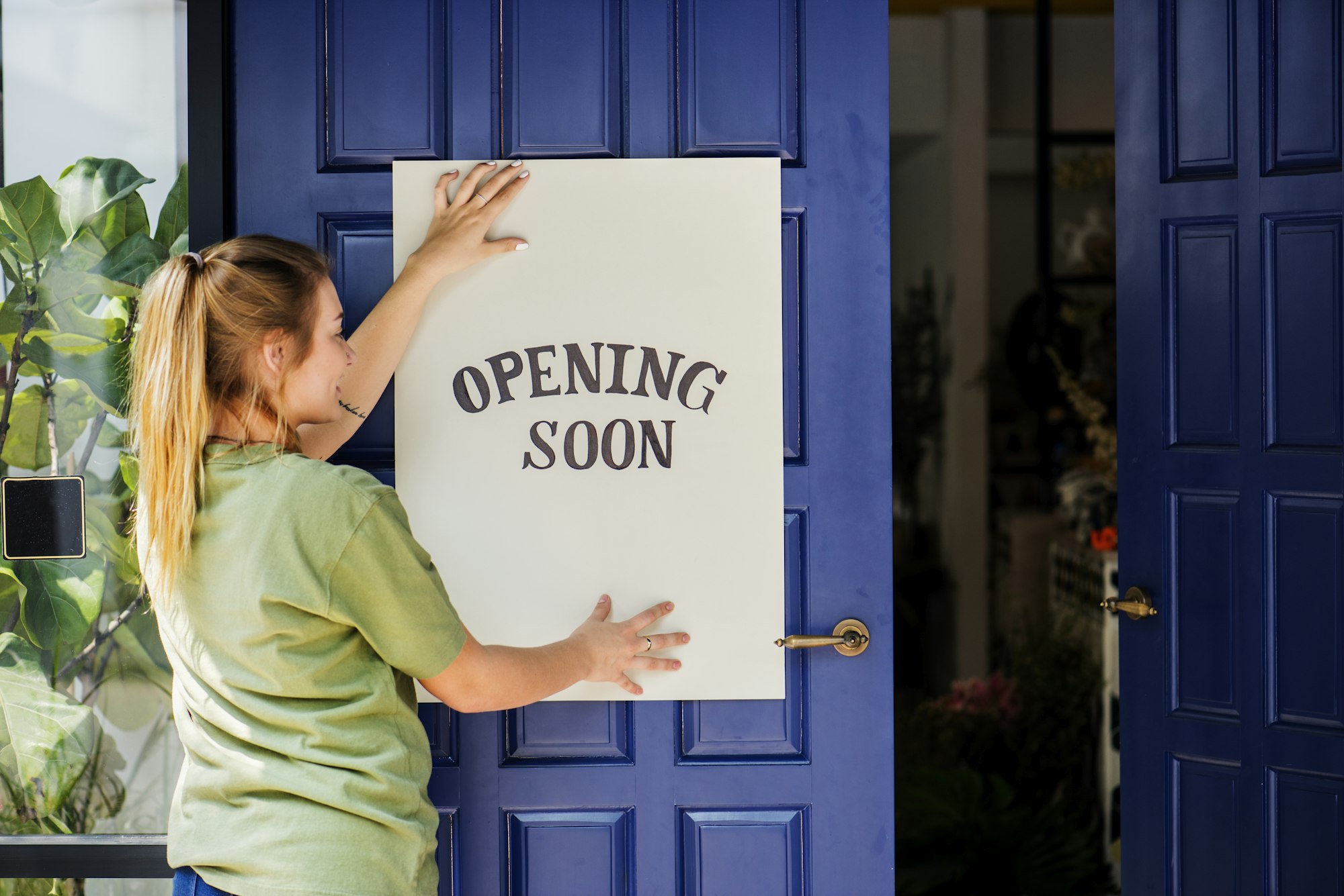 Woman putting on store opening soon sign